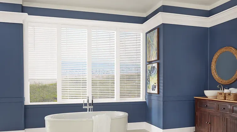 Blue dining room with white shutters, round table, and wooden sideboard under a mirror