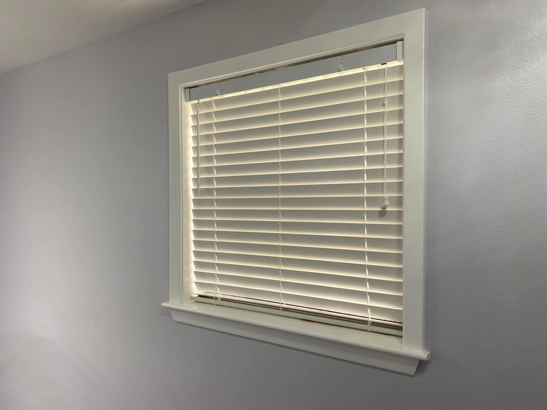 White window blinds in a light gray wall with a small sill underneath