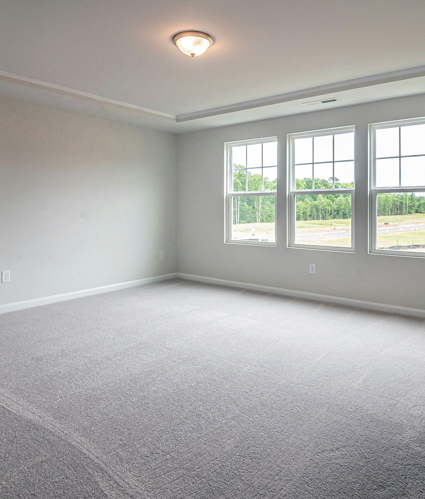 Empty room with gray carpet, three windows, and a ceiling light.