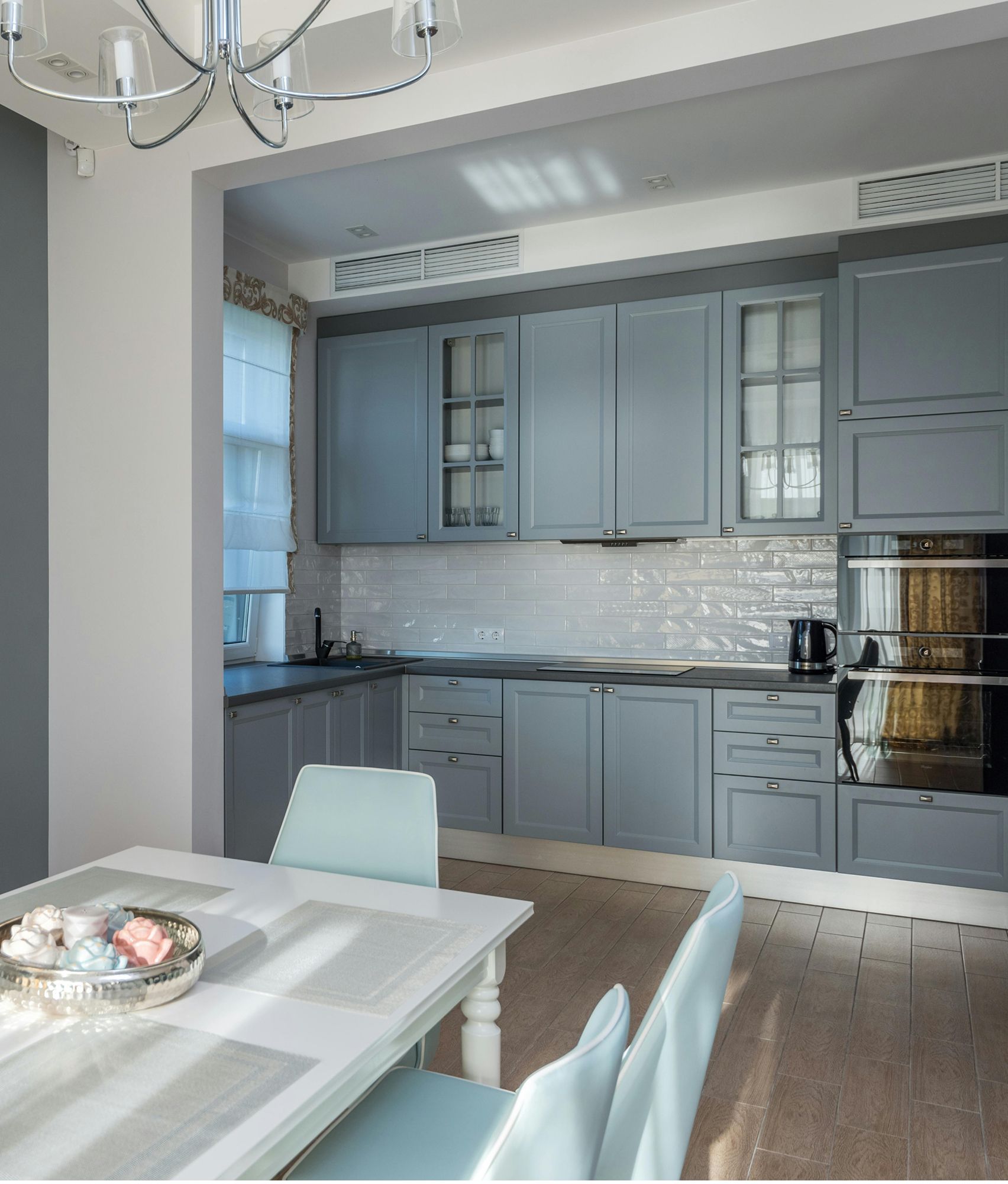 Blue kitchen with white table and chairs. Includes cabinets, oven, and a decorative tray.