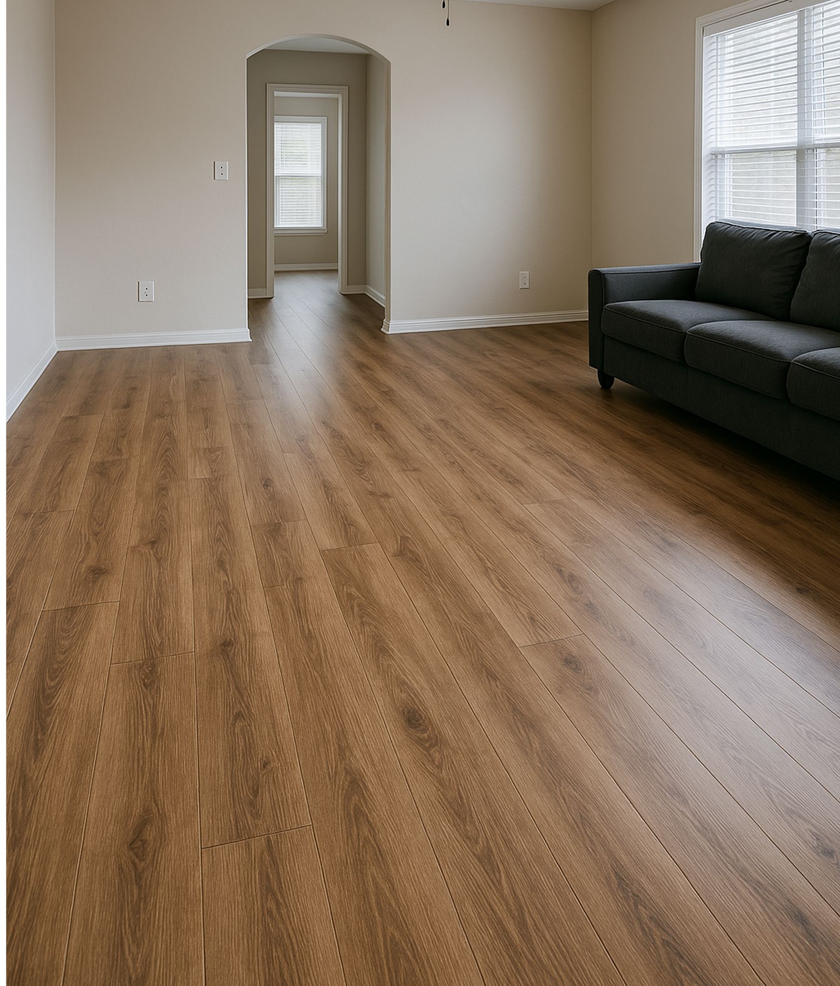 Empty living room with wood-look flooring, neutral walls, a dark gray sofa, and a window.