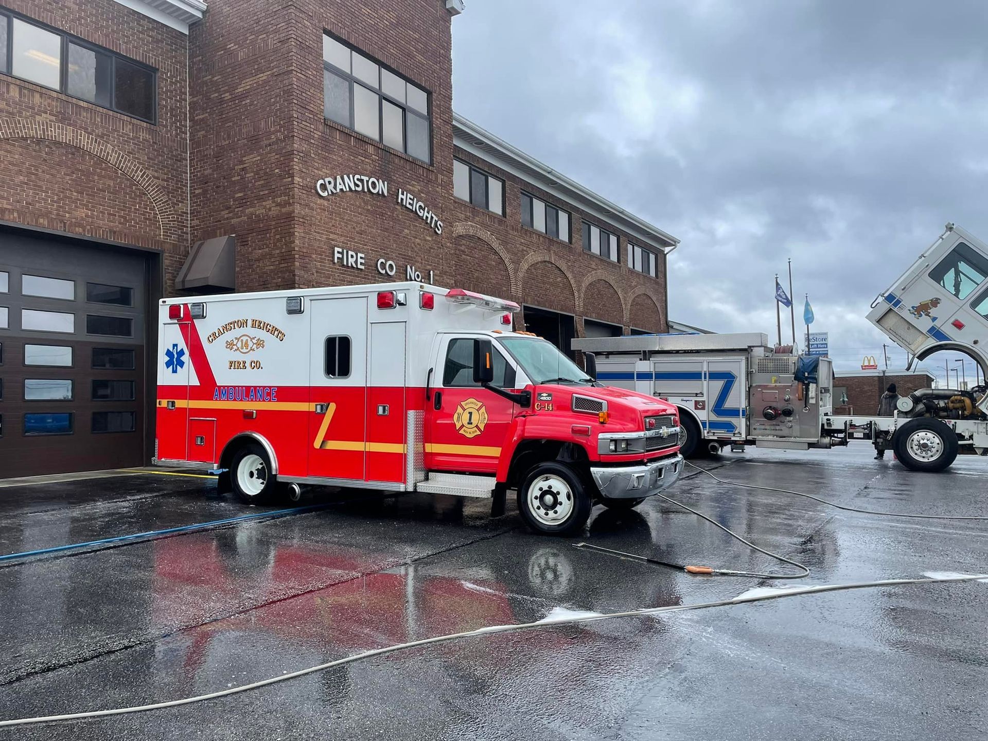 A red and white ambulance is parked in front of a fire station.