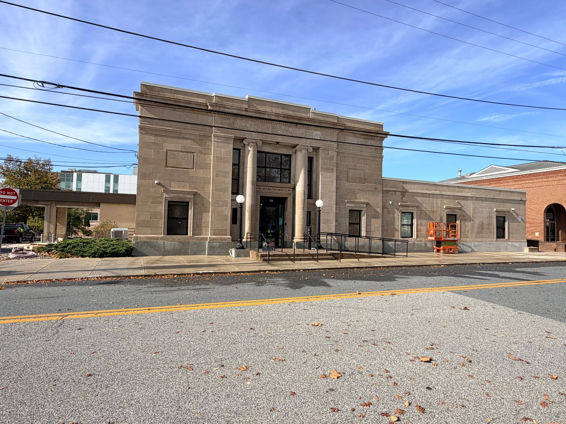 Beige bank building with columns, under blue sky, fronted by sidewalk and road.