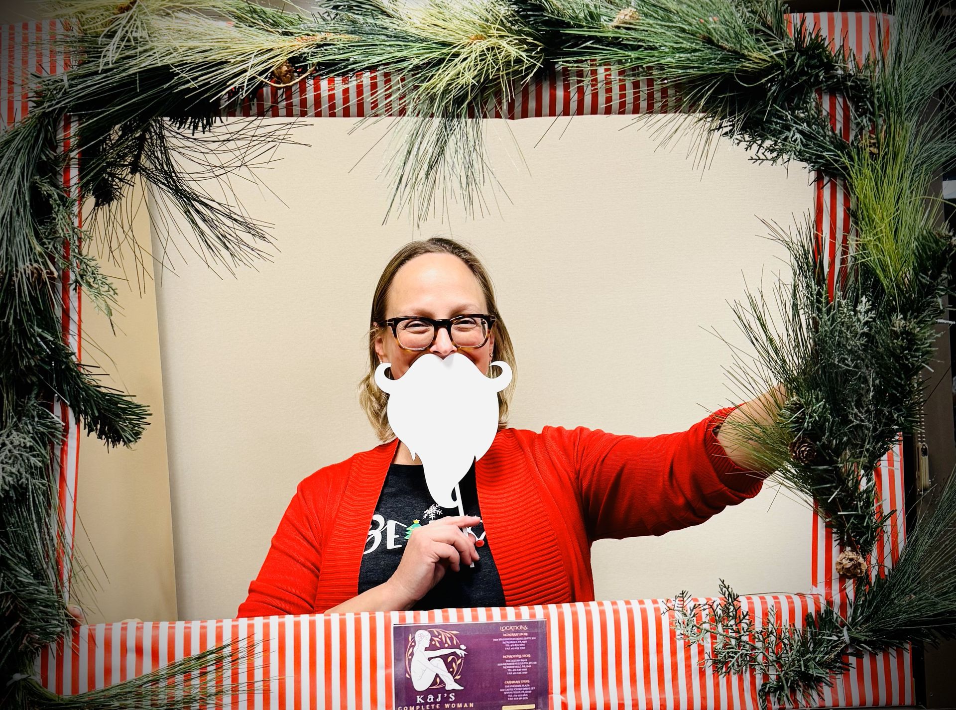 A woman is holding a fake beard in front of a picture frame.