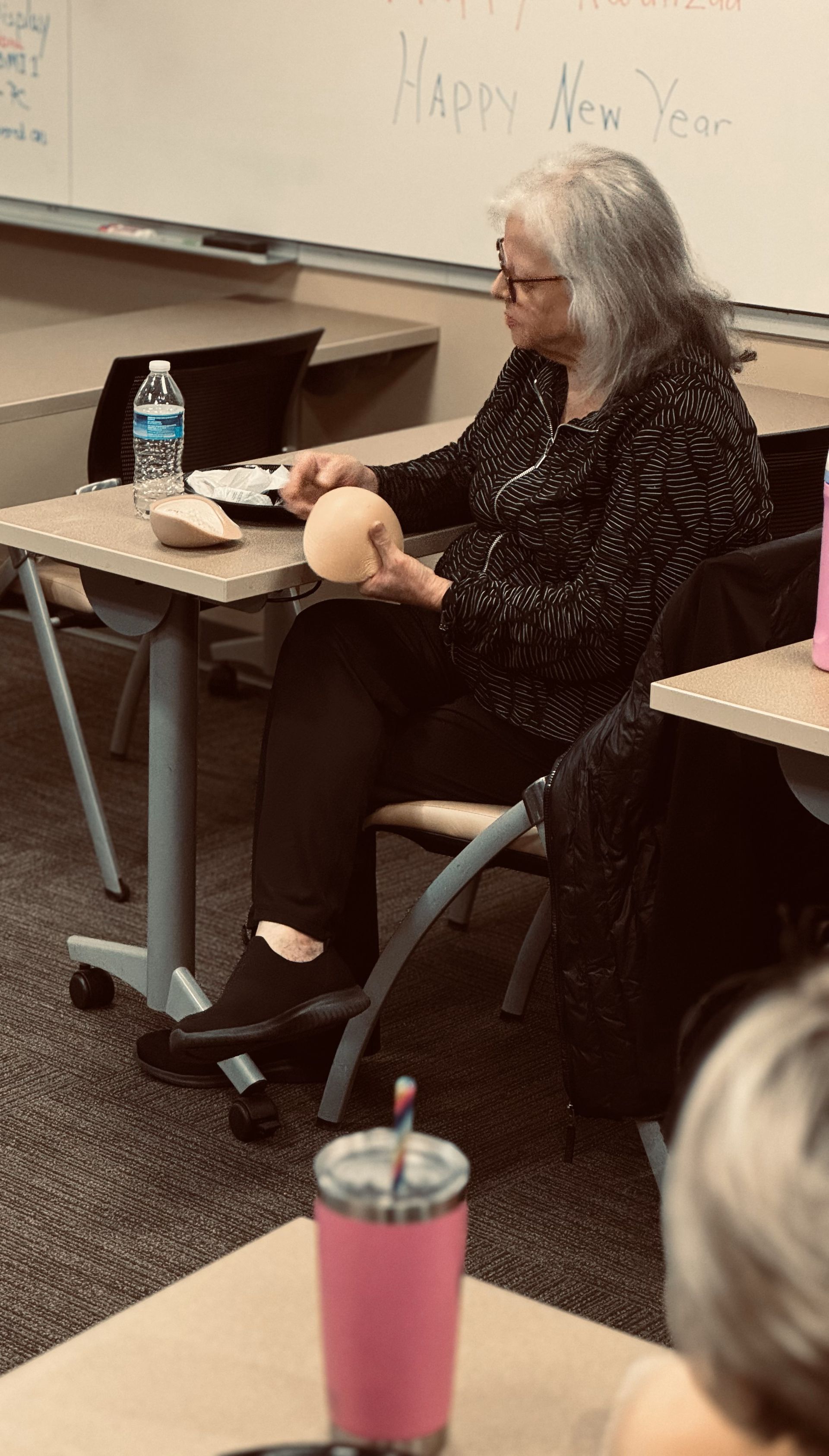 A woman is sitting at a desk in a classroom holding an apple.