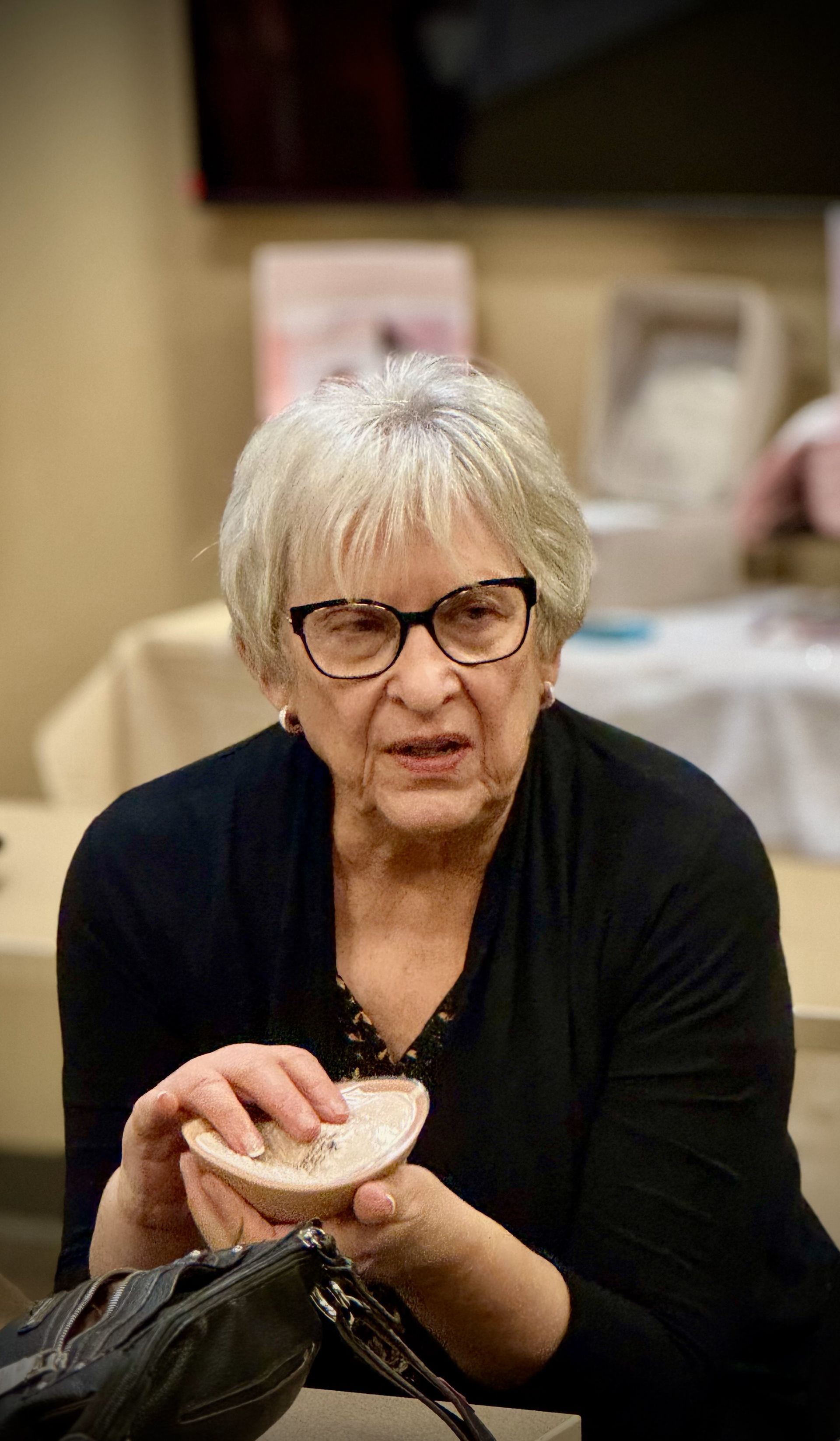 A woman wearing glasses is sitting at a table holding a piece of bread.