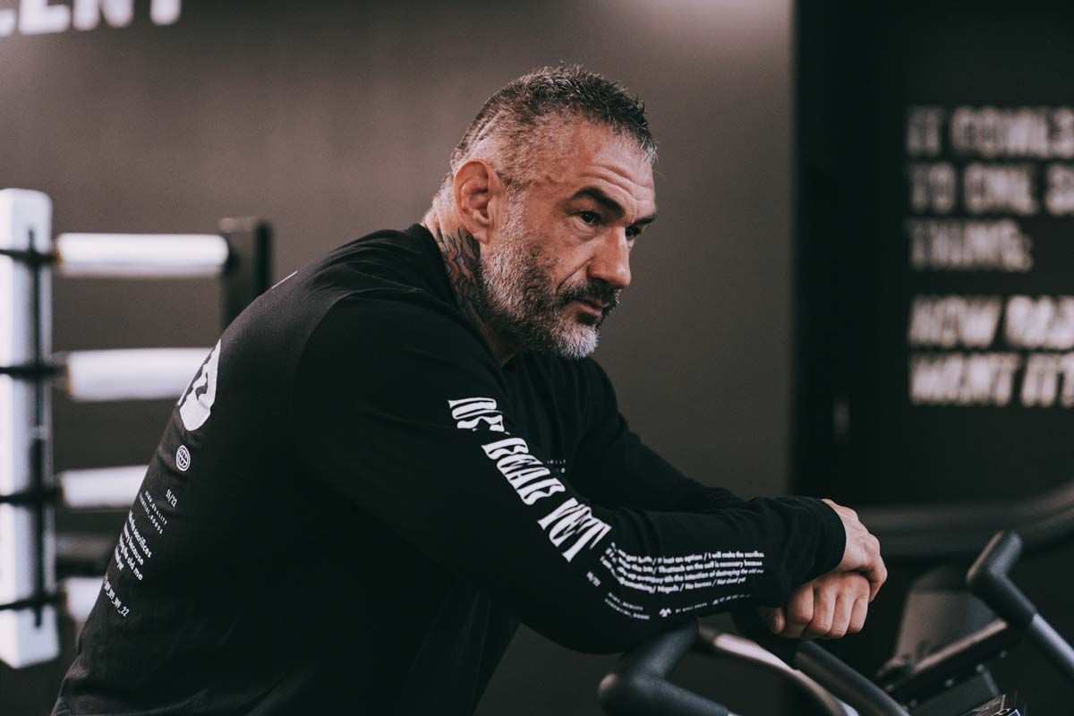 A man with a beard is leaning on a bicycle in a gym.