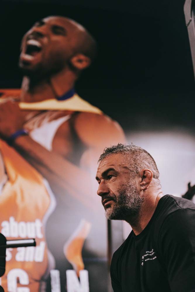 A man with a beard is standing in front of a picture of a basketball player.