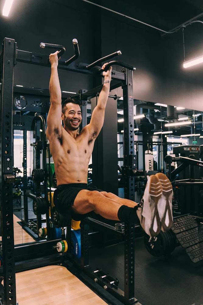 A shirtless man is doing pull ups on a machine in a gym.