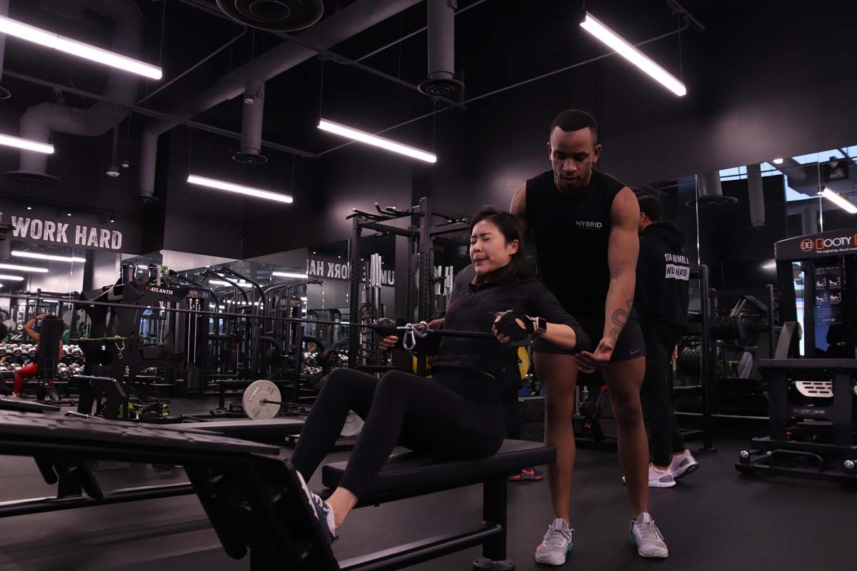 A man is helping a woman exercise on a rowing machine in a gym.