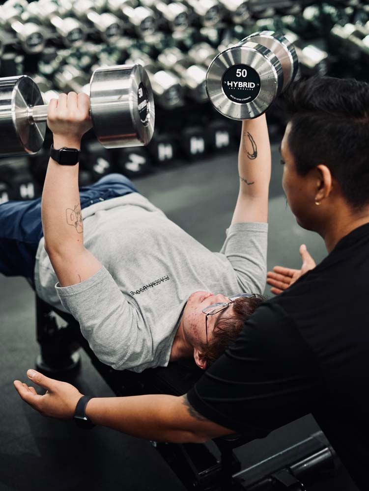 A man is lifting a dumbbell while laying on a bench in a gym.