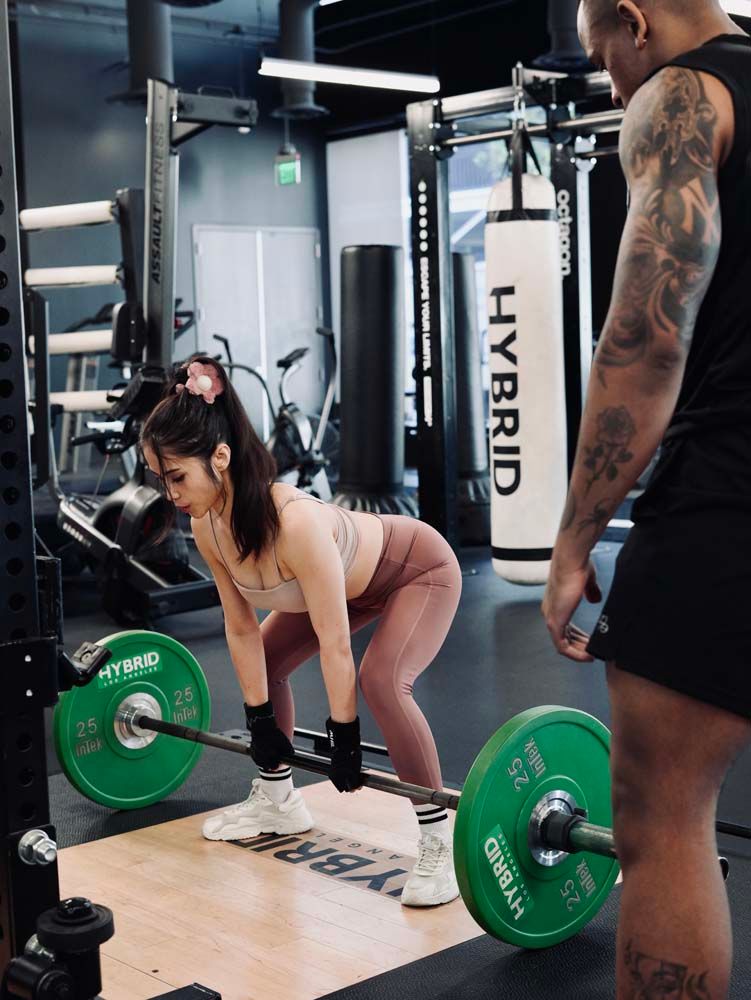 A man is watching a woman lift a barbell in a gym.