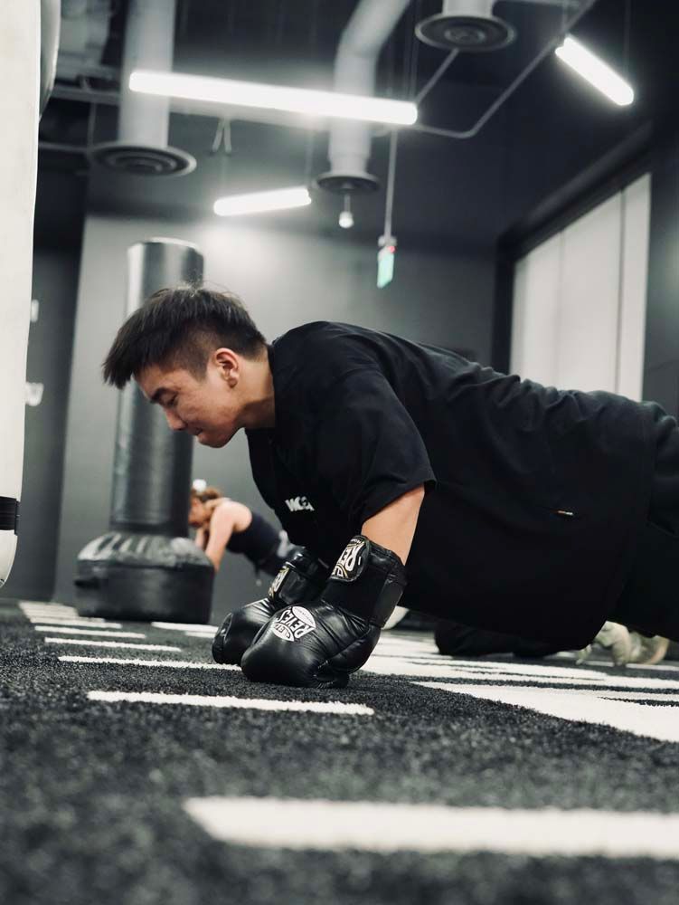 A man wearing boxing gloves is doing push ups in a gym.