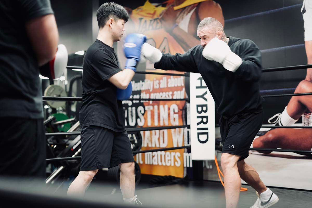 Two men are boxing in a ring with a sign that says hybrid on it