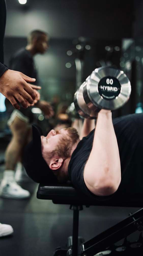 A man is lifting a dumbbell while laying on a bench in a gym.