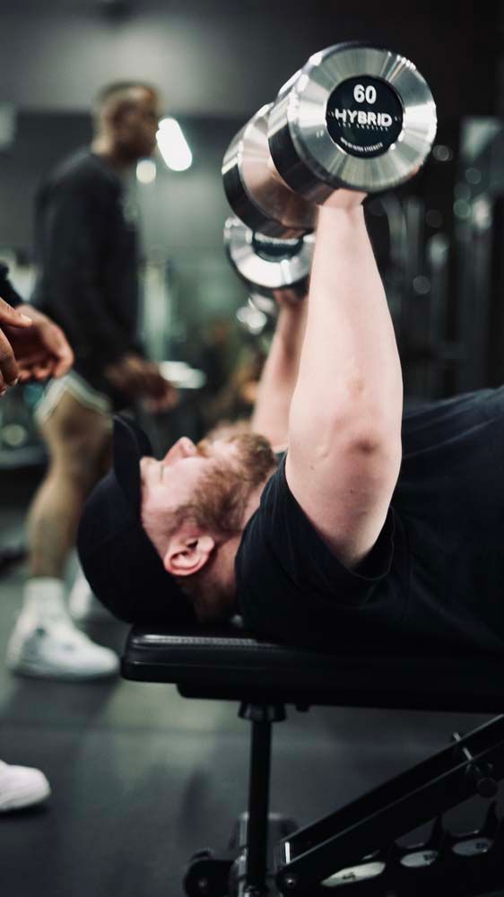 A man is lifting a dumbbell on a bench in a gym.
