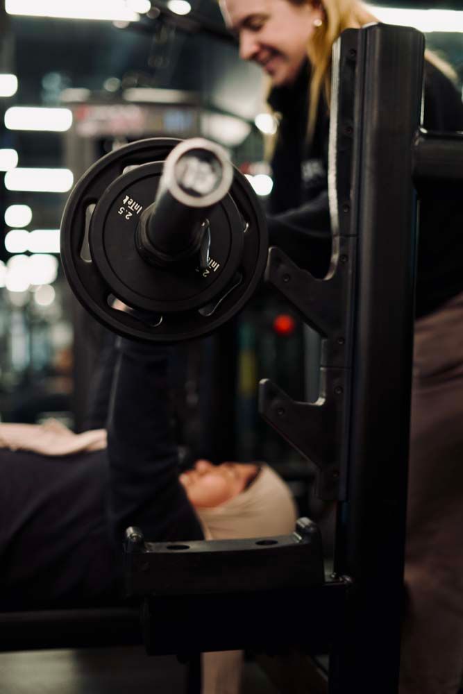 A woman is helping a man lift a barbell on a bench in a gym.