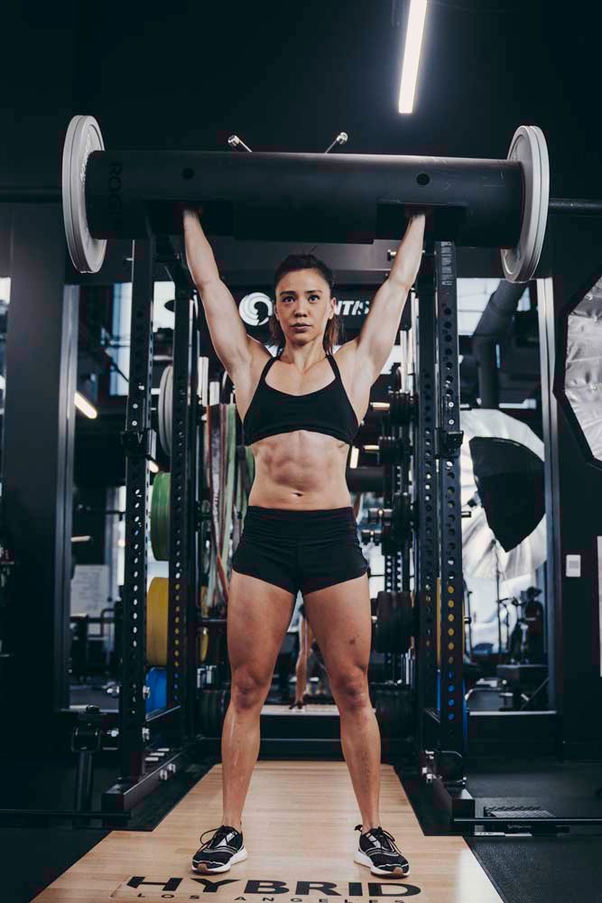 A woman is lifting a barbell over her head in a gym.