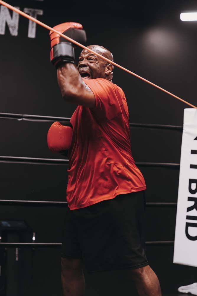 A man wearing boxing gloves is using a resistance band in a boxing ring.