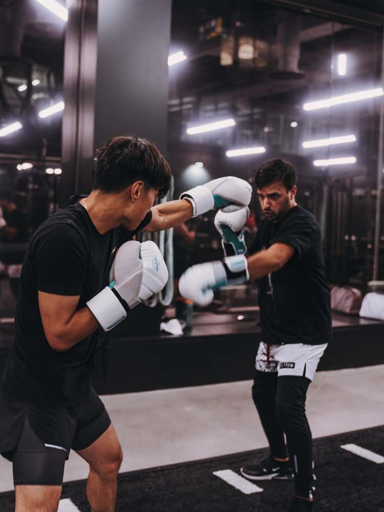 Two men are boxing in front of a mirror in a gym.