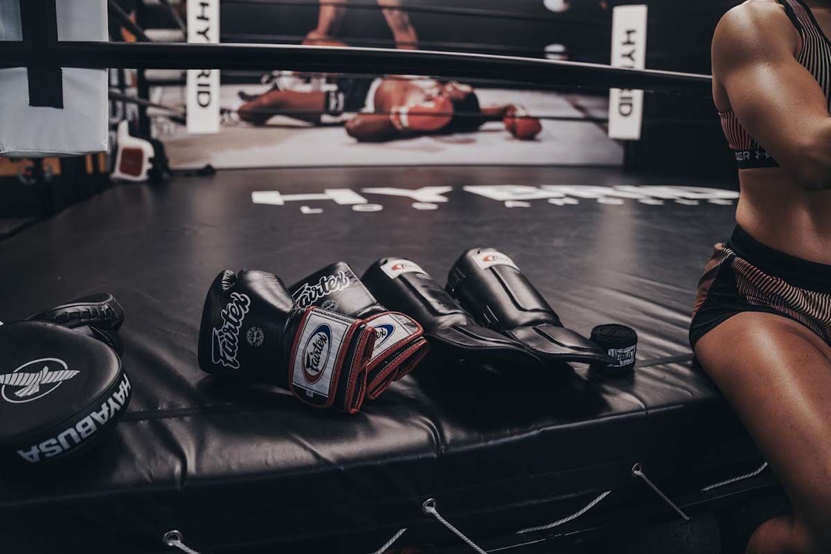 A woman is sitting in a boxing ring with boxing gloves on the floor.