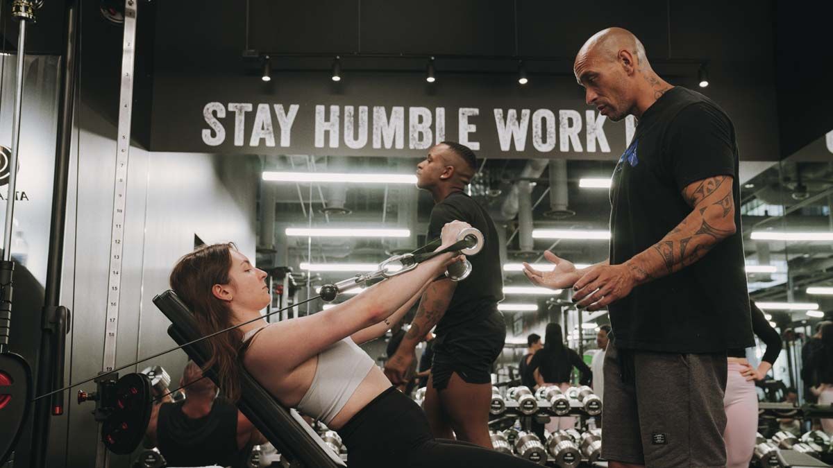 A man is helping a woman lift weights in a gym.