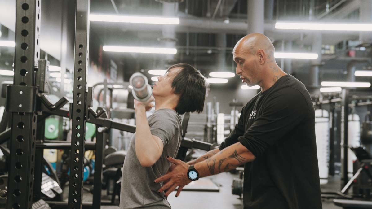 A man is helping a woman lift a dumbbell in a gym.