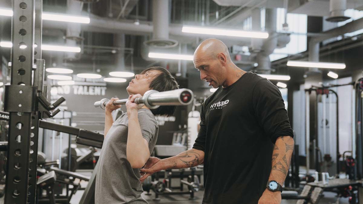 A man is helping a woman lift a barbell in a gym.