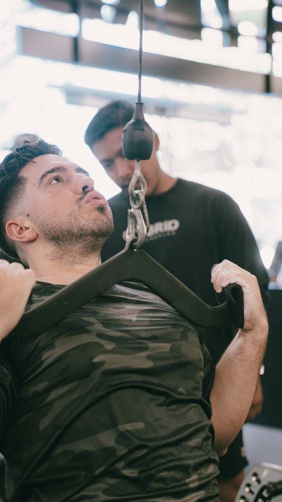 A man is using a machine in a gym while another man watches.