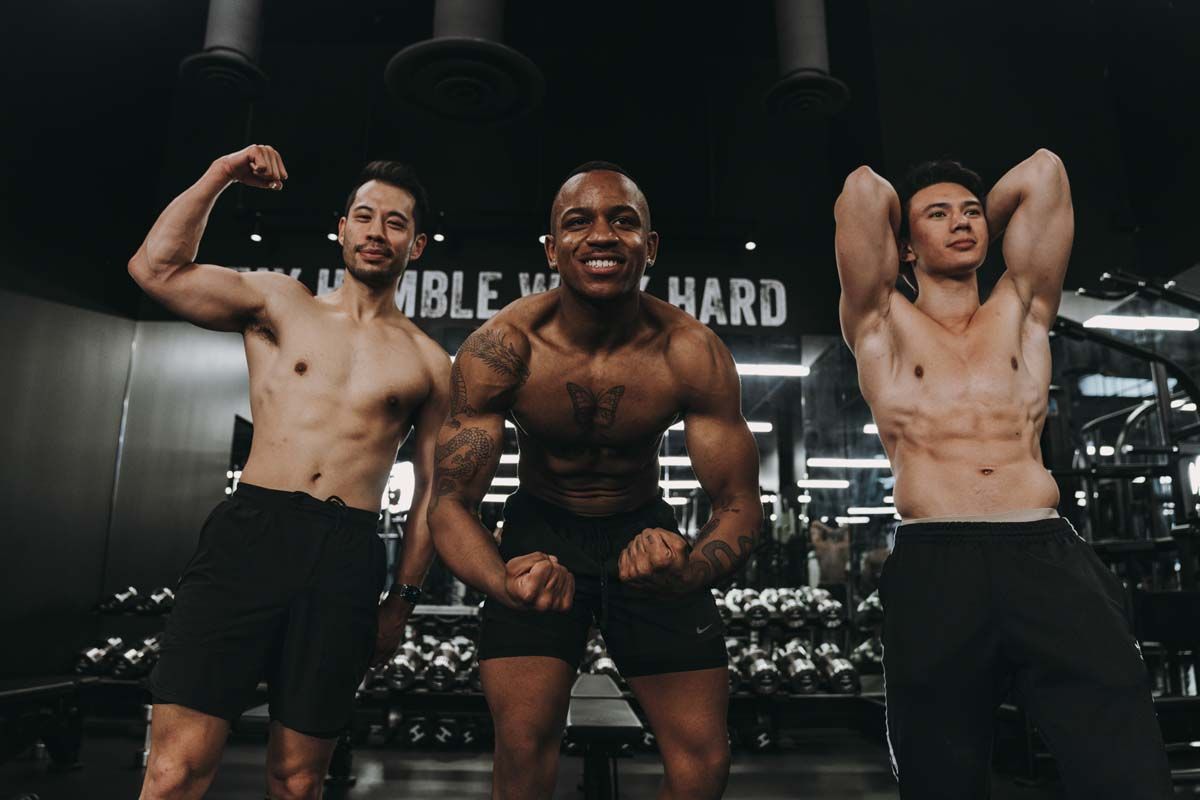 Three shirtless men are posing for a picture in a gym.