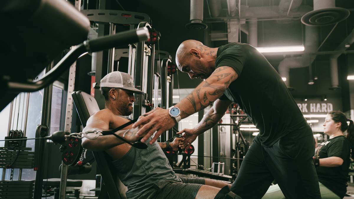 A man is helping another man lift weights in a gym.