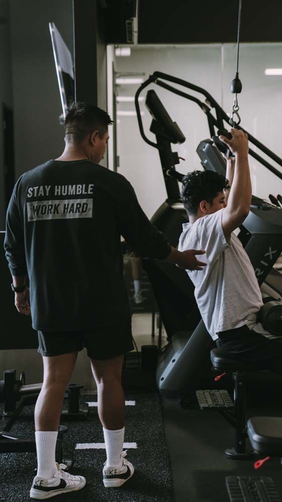 A man is helping another man lift weights in a gym.