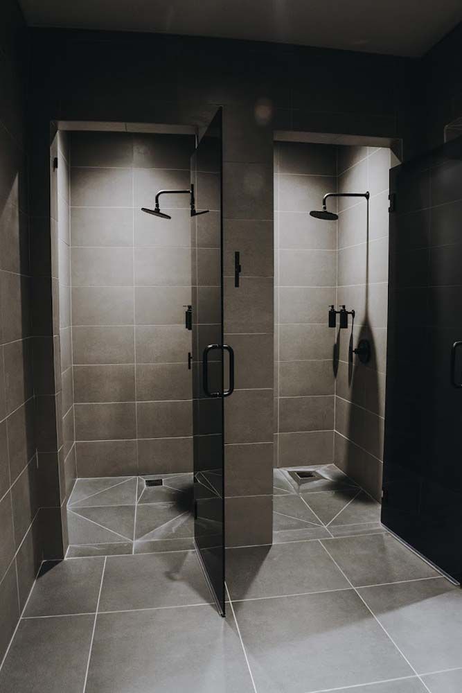 A bathroom with two showers , one of which has a glass door.