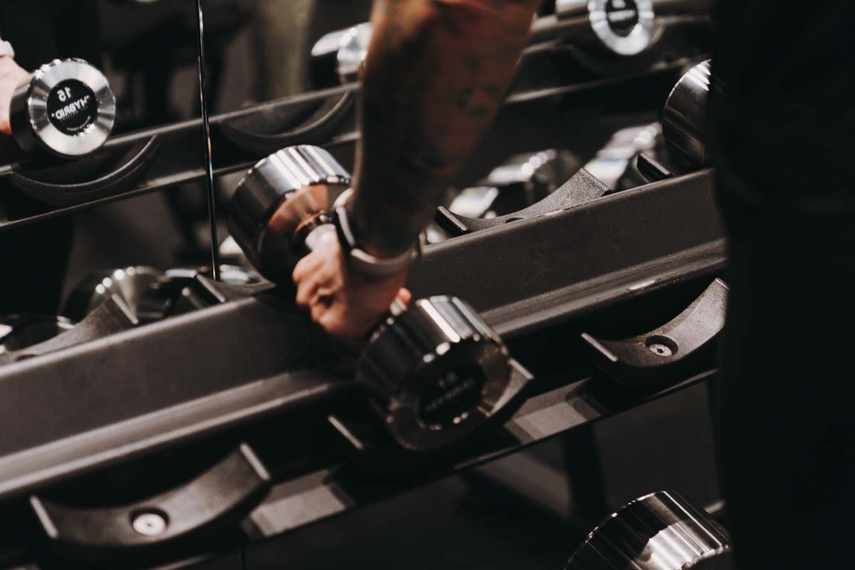A person is holding a dumbbell in front of a mirror in a gym.