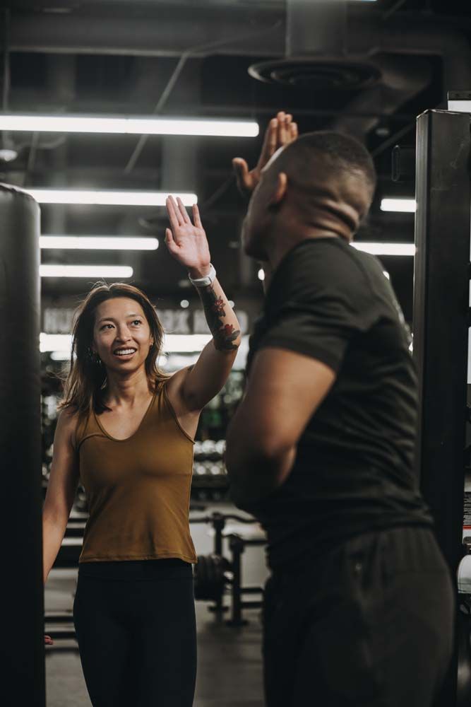 A man and a woman are giving each other a high five in a gym.