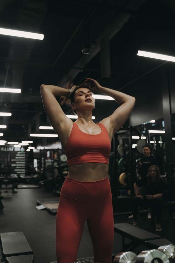 A woman in a red sports bra and leggings is standing in a gym.