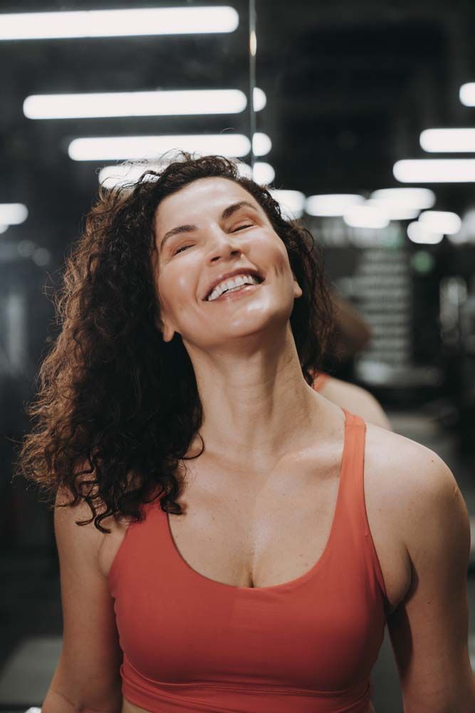 A woman is smiling in front of a mirror in a gym.