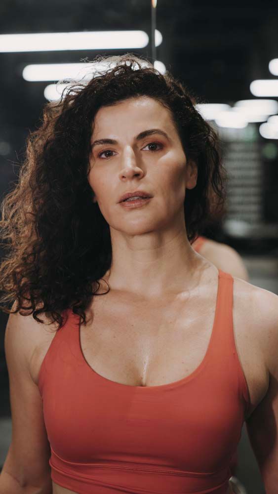 A woman in a red sports bra is standing in front of a mirror in a gym.