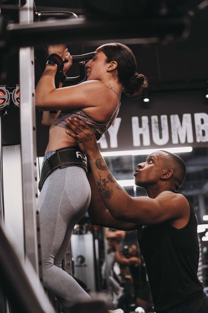 A man is helping a woman do a pull up in a gym.