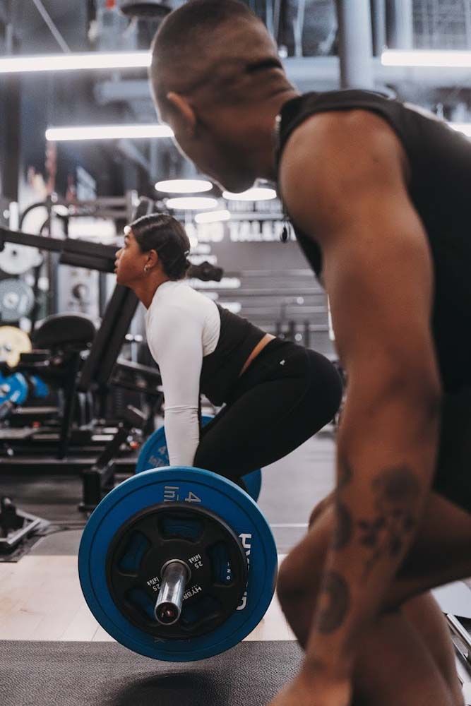 A man and a woman are squatting down with a barbell in a gym.