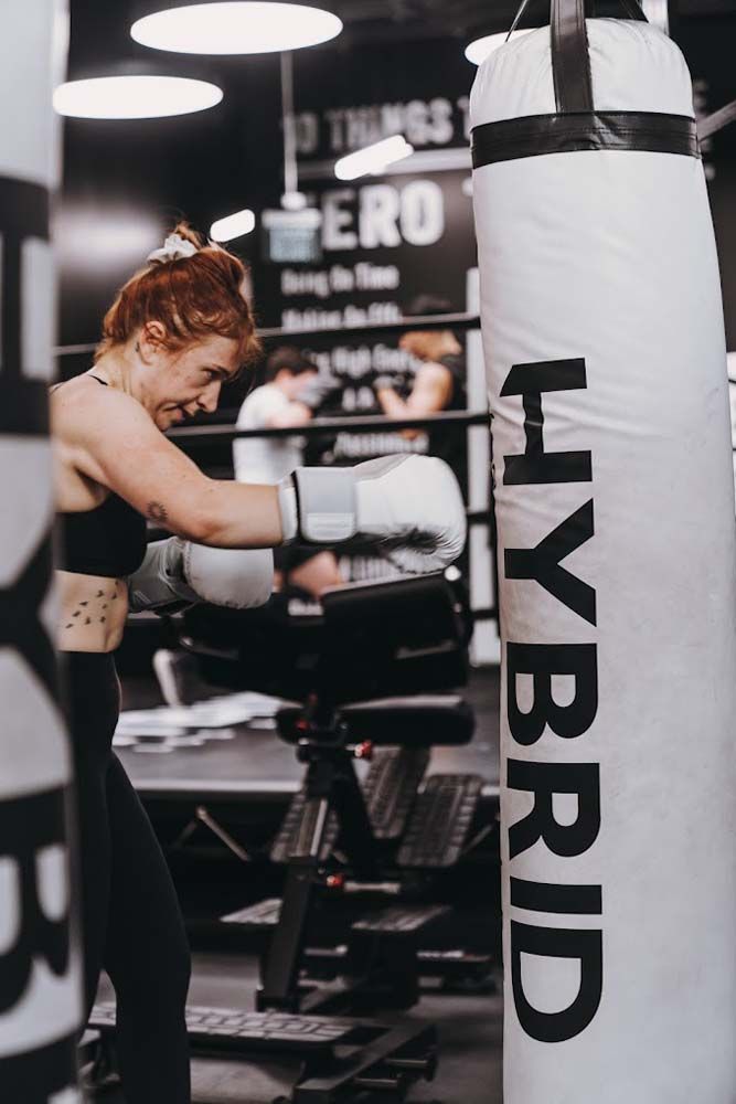 A woman is boxing in a gym next to a hybrid boxing bag.
