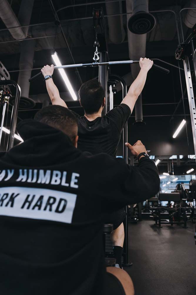 A man is doing a pull up in a gym while wearing a hoodie that says work hard.