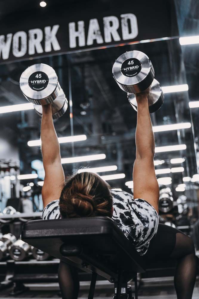 A woman is lifting dumbbells on a bench in a gym.