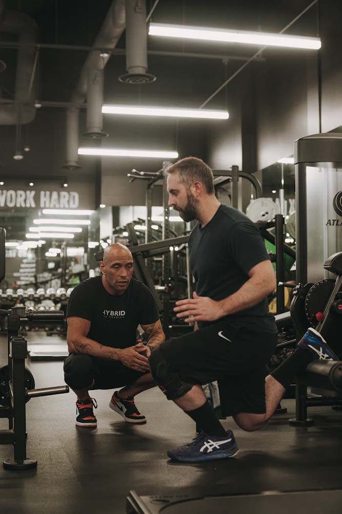 A man is squatting down next to another man in a gym.