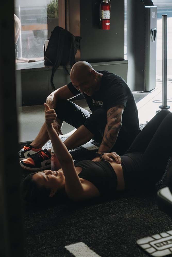 A man is helping a woman stretch her leg in a gym.