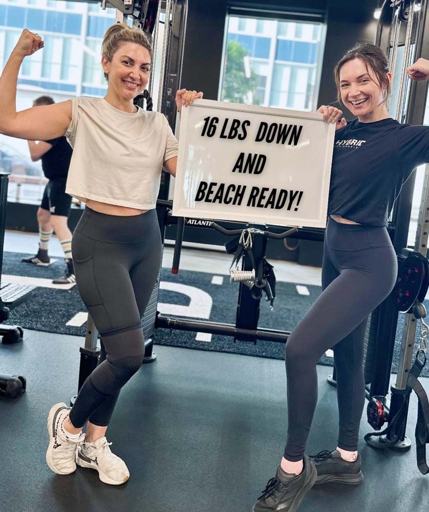 Two women are standing next to each other in a gym holding a sign that says `` 16 lbs down and beach ready ''.