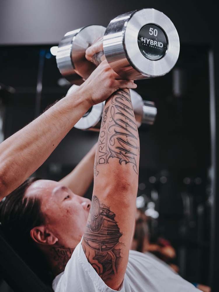 A man is lifting a dumbbell over his head in a gym.