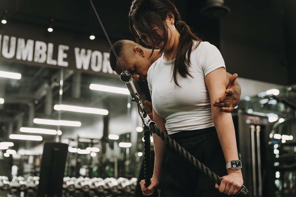 A man is helping a woman lift a rope in a gym.