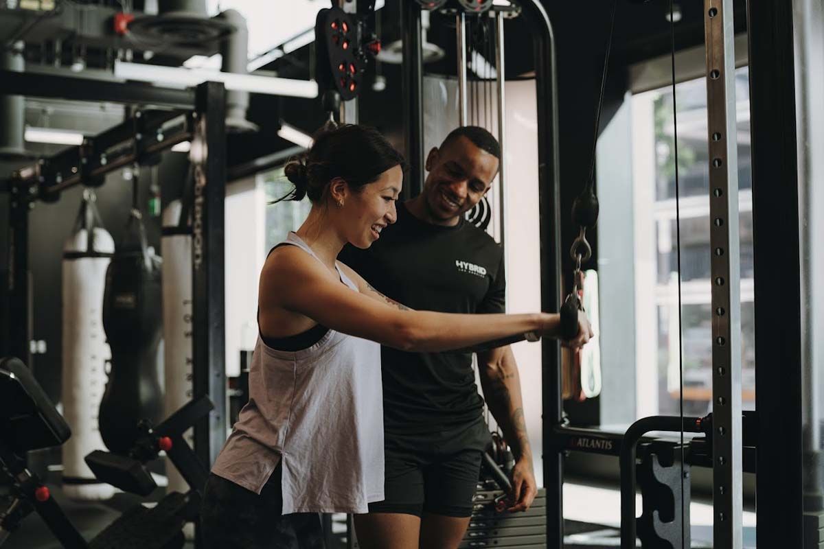 A man is helping a woman do exercises in a gym.