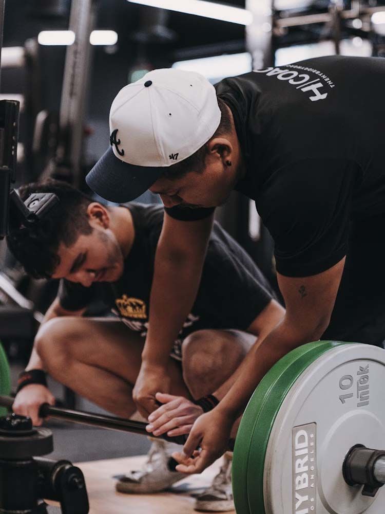 Two men are working on a barbell in a gym.